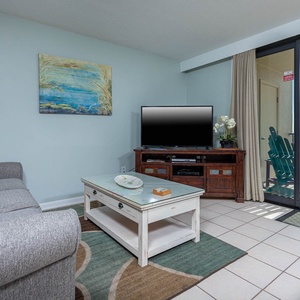 This inviting living area features a cozy sofa with queen sleeper, a large TV, and a breathtaking beach view from the balcony