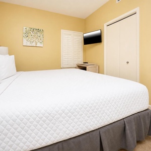 A cozy bedroom features a plush king bed, a wall-mounted TV, and soft yellow walls, creating a warm and inviting atmosphere