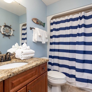 The bathroom features a stylish granite countertop, nautical decor, and striped shower curtain for a refreshing coastal vibe
