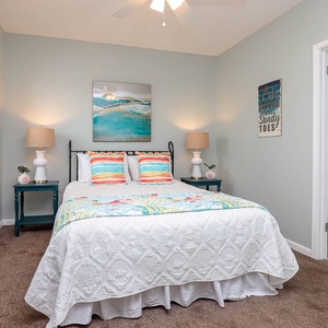 Cozy guest bedroom features a queen bed adorned with colorful pillows, soft lighting, and beach decor for a relaxing stay
