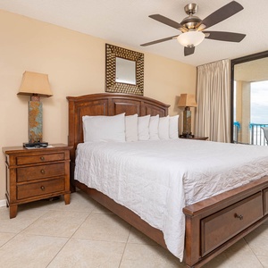The cozy master suite features a king bed with plush pillows, a stylish nightstand, and a balcony offering a beach front view