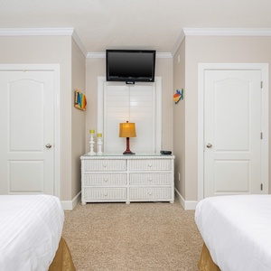 This guest bedroom features two double beds, a dresser with a lamp, and a wall-mounted TV for relaxation