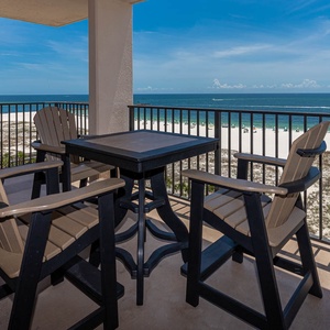 Savor the view from the balcony, featuring a table and chairs perfect for enjoying drinks while overlooking the shore