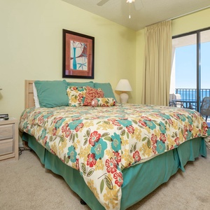 Master bedroom featuring a king bed, cozy nightstand, and a balcony view of the beach beyond the sliding doors