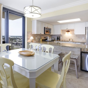 Dining space featuring a glass-top table with yellow chairs, complemented by a modern kitchen and access to the balcony