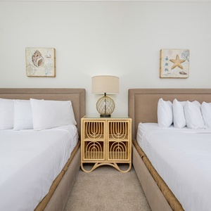 Guest bedroom featuring two queen beds, decorative coastal art, and a stylish lamp on a stylish nightstand