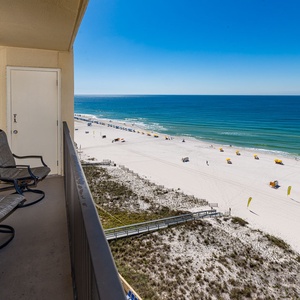 The balcony features a lounge chair with a view of the beach, lined with umbrellas and sunbathers enjoying the shoreline