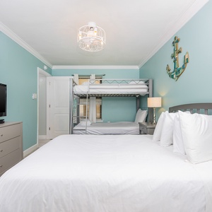 This guest bedroom features a full bed, a twin bunk bed, a TV, and soft blue walls, creating a relaxed coastal atmosphere