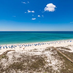 You watch colorful umbrellas dot the white sand while the calm coast extends to meet the sky