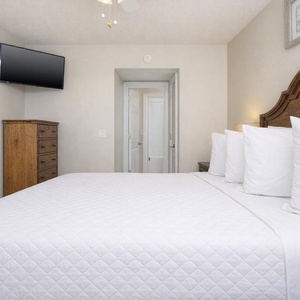 This cozy bedroom features a wooden headboard, a mounted TV, and a serene atmosphere perfect for relaxation