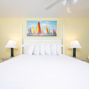 Brightly colored sailboat artwork complements the inviting white bedding and cozy lamps in this cheerful master suite retreat