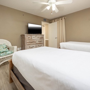 This cozy guest bedroom features two beds, a stylish dresser, and a relaxing wicker chair, perfect for unwinding