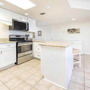 Bright kitchen features white cabinetry, granite countertops, and a breakfast bar with seating, leading to a cozy living area