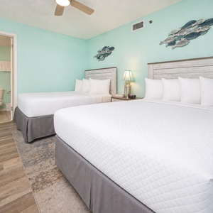 Bright guest bedroom featuring two double beds, a soothing aqua wall, and a cozy lamp beside a nightstand
