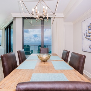 Large wooden dining table with comfortable seating, with coastal artwork and views of the inviting balcony