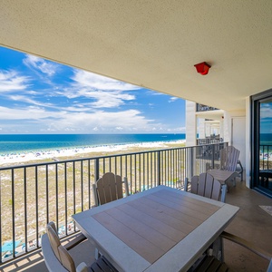 Spacious balcony with a dining table and chairs offers stunning views of the beach and vibrant blue gulf waters