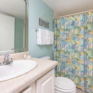 The bathroom features a colorful seashell shower curtain, a sleek sink, and fresh towels for a beach-inspired retreat