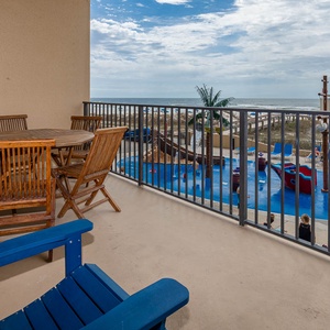 The balcony features a round dining table and wooden chairs, overlooking the beach and pirate ship splash park