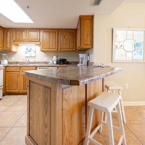 Warm wood cabinetry complements the kitchen's countertop, featuring a breakfast bar with white stools