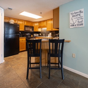 A cozy kitchen features wooden cabinetry, black appliances, Keurig, coffee maker, and a bar area with black chairs