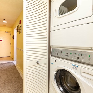 A convenient laundry area features a stacked washer and dryer, with a bright yellow hallway leading to the entrance