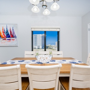 Gather around the inviting dining table, accented by a colorful sailboat painting and a view through the window