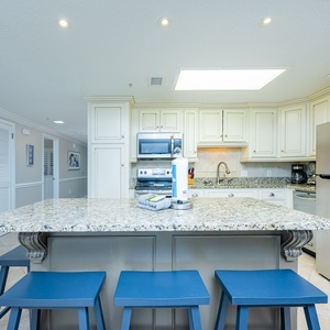 Gather around the spacious granite island with blue stools, perfect for casual meals and conversations in the kitchen