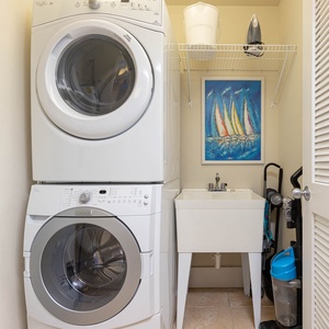Bright laundry room featuring a stacked washer and dryer, utility sink, and colorful sailboat artwork for a cheerful touch