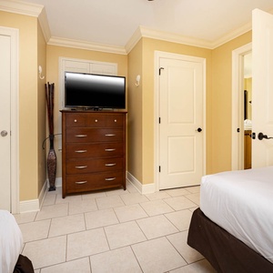 Guest room featuring two double beds, a wooden dresser with a TV, and a warm, inviting color scheme