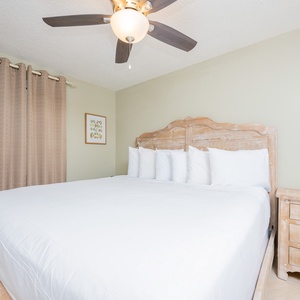 Bright and airy guest bedroom featuring a king bed with plush white bedding, wooden furniture, and soft beige curtains