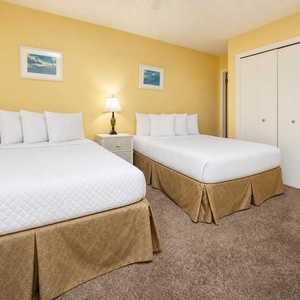 Cozy guest bedroom featuring two full beds, soft carpeting, and cheerful yellow walls