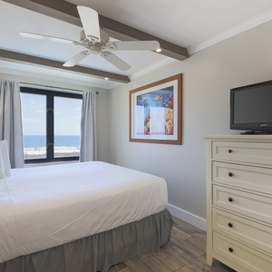 This bedroom features a cozy atmosphere with a large window offering a beachfront view and a TV for entertainment
