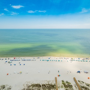 Take in the vibrant beach scene with colorful umbrellas and people enjoying the water, creating a lively atmosphere