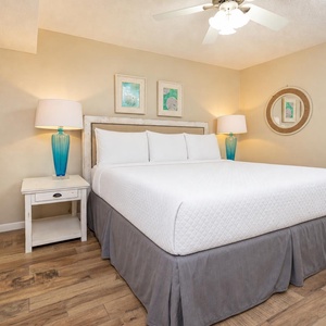 Bright bedroom featuring a king bed with a gray skirt, two blue lamps, and charming coastal artwork on the walls