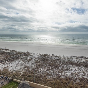 A serene view of a white sand beach stretches along the coastline, framed by gentle waves and a blue sky