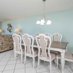 A stylish dining area features a light wood table surrounded by elegant white chairs, complemented by a colorful sofa