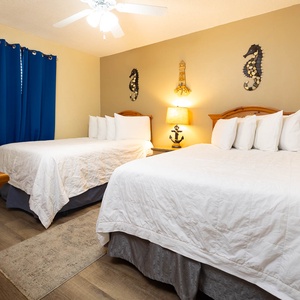 This guest bedroom features two double beds, blue curtains, nautical decor, and warm lighting for a cozy atmosphere