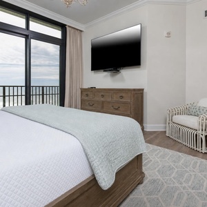 The master bedroom features a cozy king bed, a large TV, and beachfront views from the balcony door