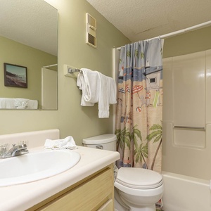 This bathroom features a light green color scheme, a spacious vanity, and a playful beach-themed shower curtain