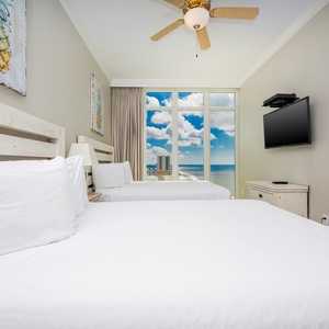 Enjoy restful nights in this inviting guest bedroom with two queen beds, a TV, and beautiful beach views