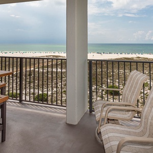 Balcony seating with a dining table offers a view of the beach and vibrant umbrellas lining the shore