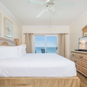 The master bedroom features a large bed, a TV, and beautiful views of the beach through sliding glass doors