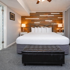 King suite featuring a stylish wooden accent wall, plush bedding, and a chic ottoman for added comfort