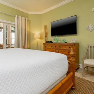 The master bedroom features soft green walls, a TV, and a lovely view of the dining area through glass doors