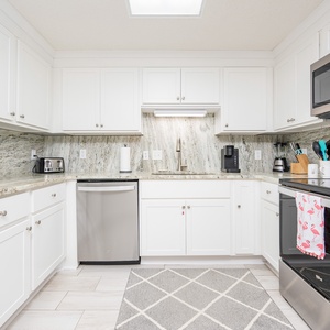 Bright white cabinetry complements the sleek countertops in this kitchen, featuring a coffee maker and stainless appliances