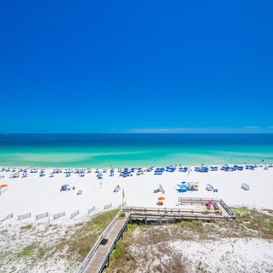 A wooden boardwalk guides you across dunes to cool waters where families gather beneath umbrellas on white sand