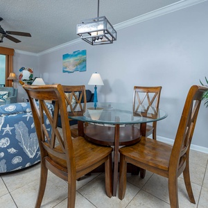 Dining area features a glass-top table with wooden chairs, complemented by a view of the beach through large windows