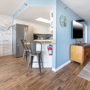 Kitchen area features a granite breakfast bar with seating, stainless steel appliances, and coastal decor accents