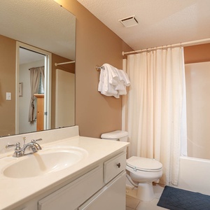 Guest bathroom featuring a sink with a large mirror, a tub/shower combo, and neatly arranged towels on a rack