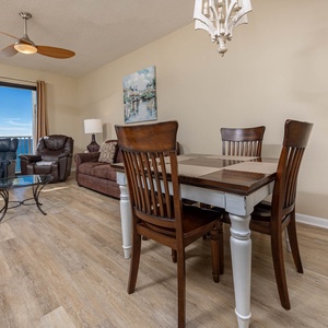 Cozy living area features a dining table, plush seating, and large windows offering a beautiful view of the gulf